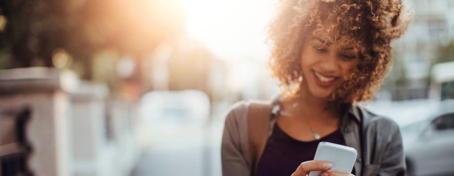 woman texts on her phone as she walks through the city